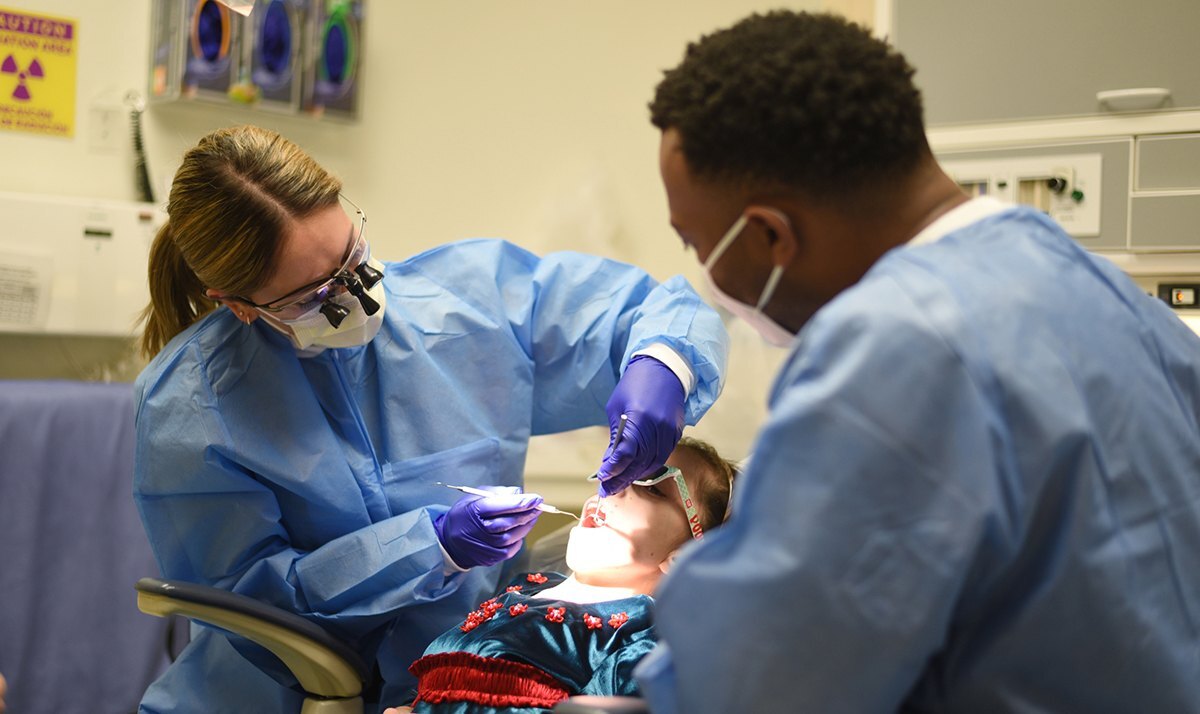 A student checks a child's mouth using high-tech dentistry equipment.