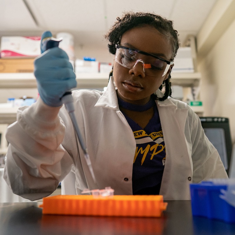 African American woman in a lab coat makes drops using a test tube.