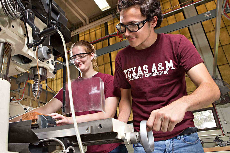 Two students smile while working with a powered wood drill.