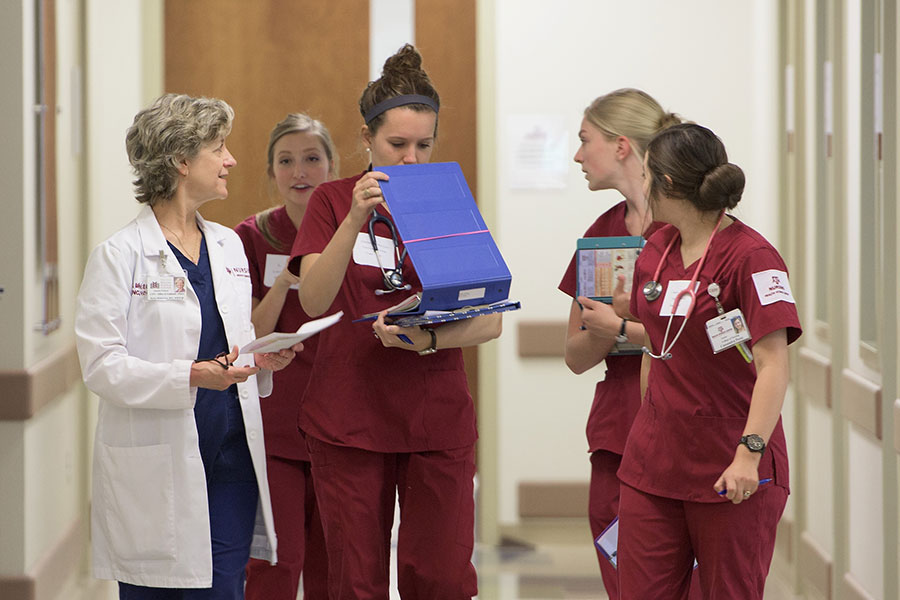 Student nurses walk and talk with a doctor as they look through charts.