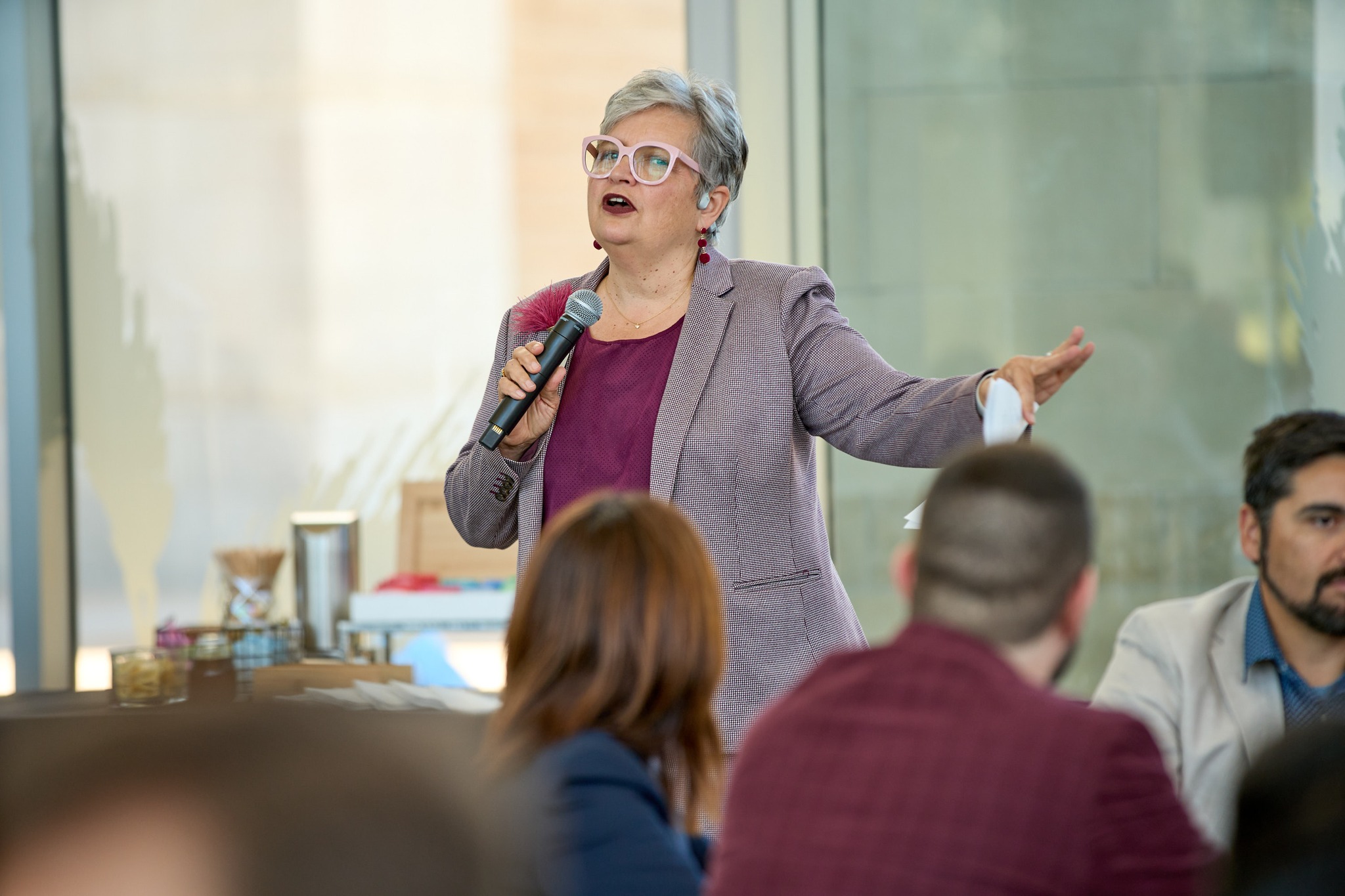 A faculty leader speaks into a handheld microphone during a professional development session, gesturing while addressing seated faculty members in a bright, modern meeting space.